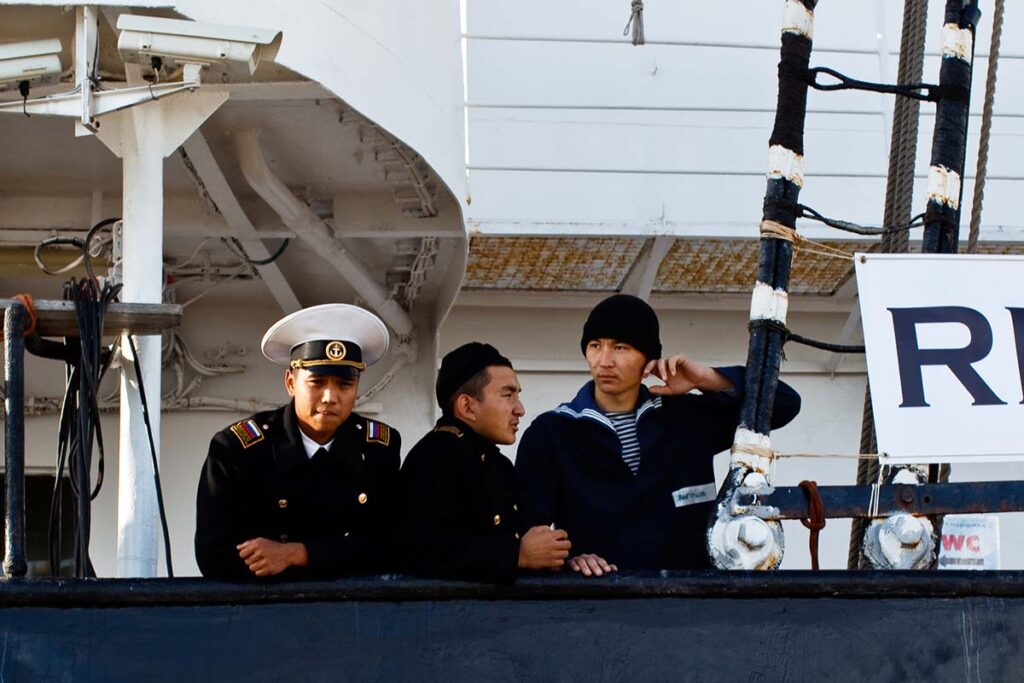 Three sailors in uniform standing on the deck of a ship, gazing outward.