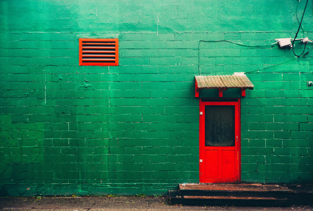 Vibrant contrast of a red door against a green wall captured through street photography on Commercial Drive, Vancouver with a Leica M-D (Typ 262) and a Canon 50mm f/1.4 LTM lens.