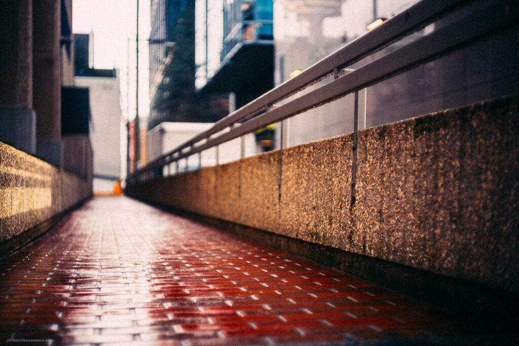Wet, reflective bricks of a Vancouver walkway glisten under the soft light, guiding the eye through the architectural lines of the cityscape.