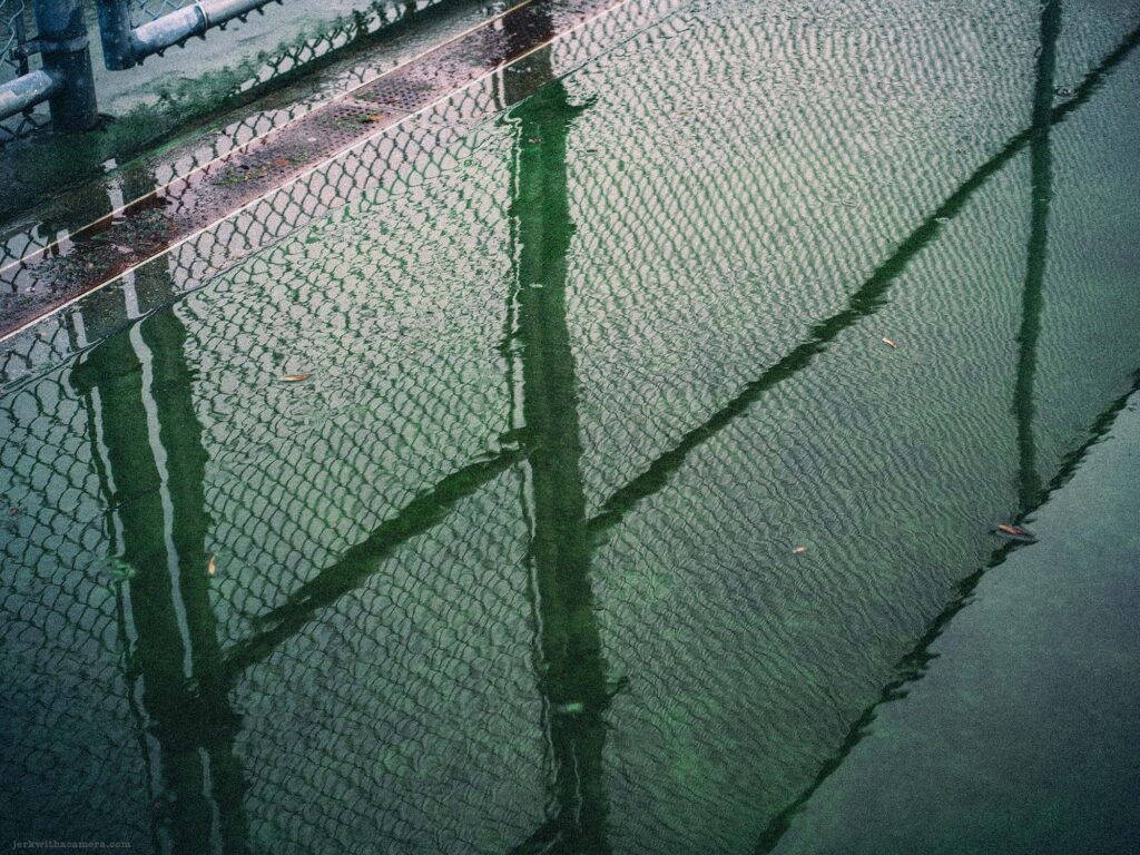 Rain-soaked tennis court with net reflecting on the wet surface, capturing the tranquility of an urban park in the rain