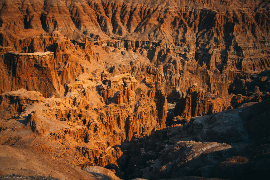 A dramatic desert canyon illuminated by warm sunlight, with winding paths carved through its rugged terrain.