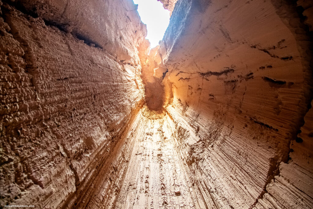 Looking up through towering rock formations with vivid blue sky above, illuminated by the warm glow of sunlight.