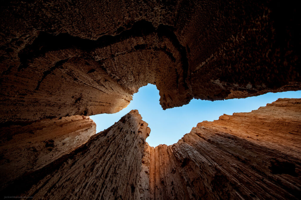 Looking up through towering rock formations with vivid blue sky above, illuminated by the warm glow of sunlight.