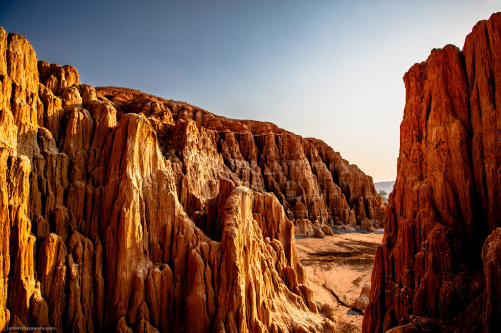 Looking up through towering rock formations with vivid blue sky above, illuminated by the warm glow of sunlight.