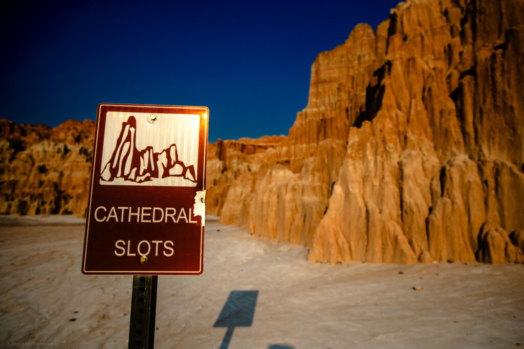 This image captures the awe-inspiring view of a canyon as seen from below, looking up towards the vivid blue sky. The rugged rock formations are bathed in golden light, emphasizing their dramatic textures and height. The perspective invites viewers to imagine standing in the canyon, surrounded by its natural grandeur.