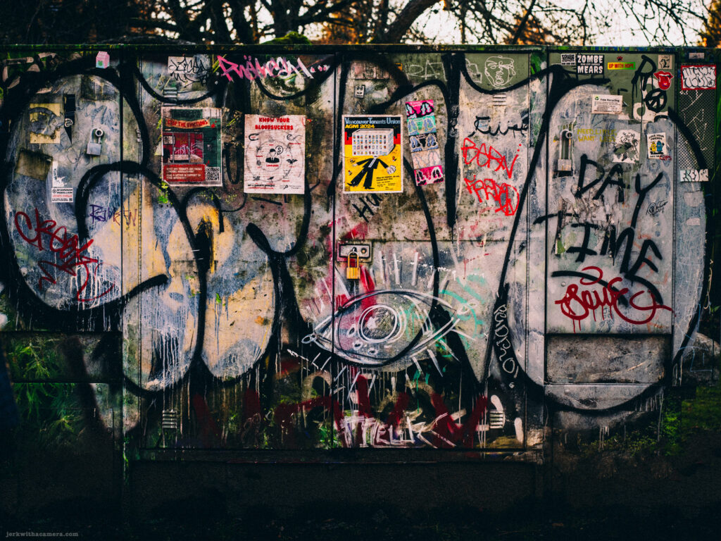 A weathered and graffiti-covered utility box surrounded by urban decay.