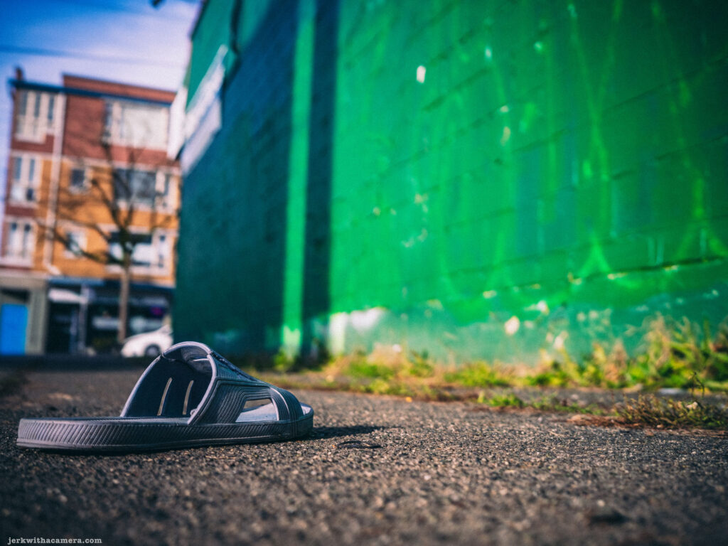 Lost sandal resting on an asphalt alley with a vibrant green wall in the background