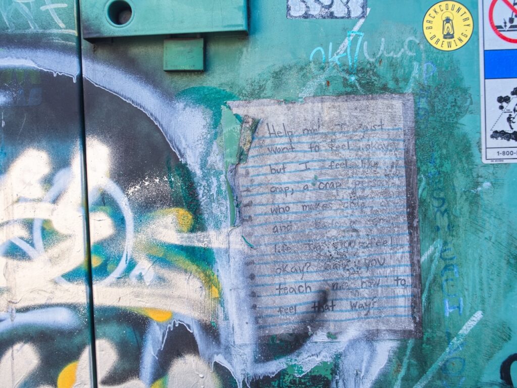 Graffiti-covered Dumpster with a handwritten note attached.