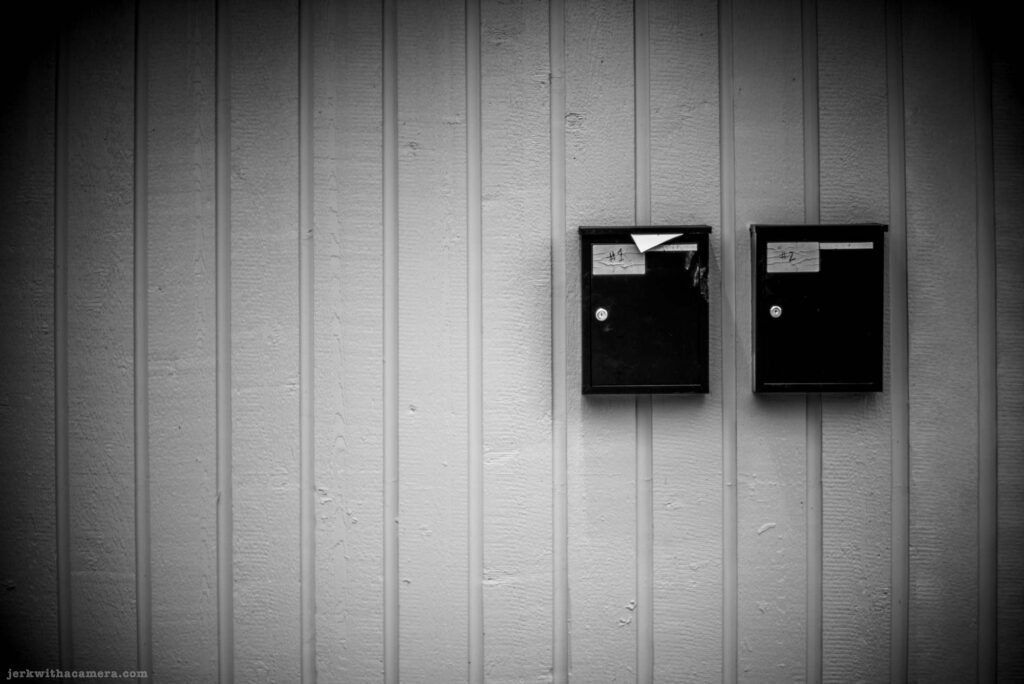 Two black wall-mounted mailboxes labeled number 1 and number 2 on a vertical siding wall