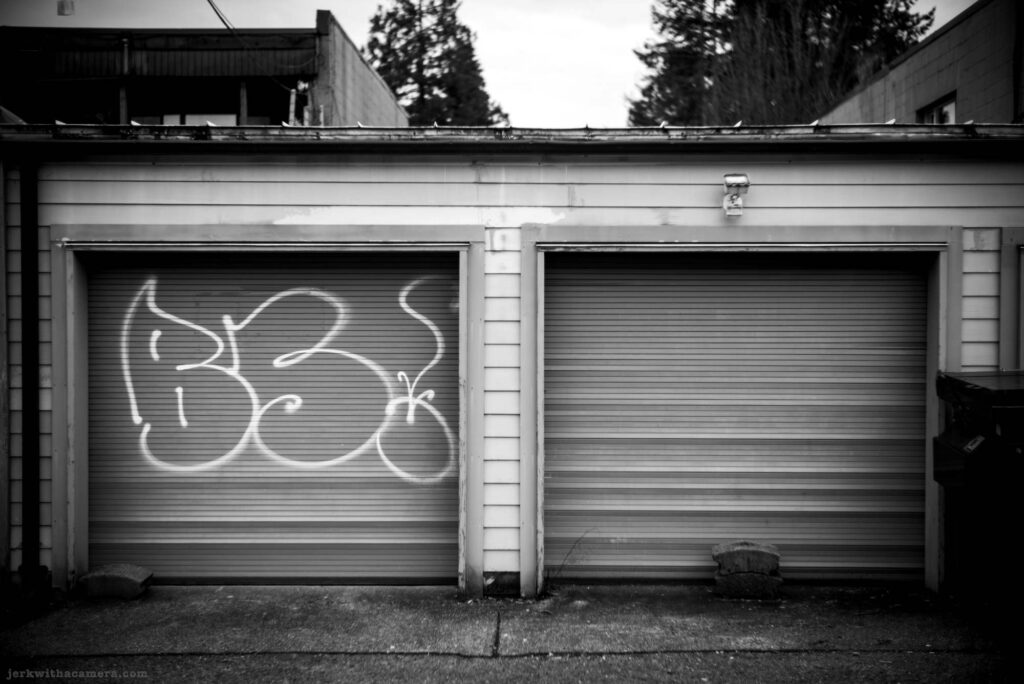 Two garage doors with graffiti on one door and concrete blocks at the base