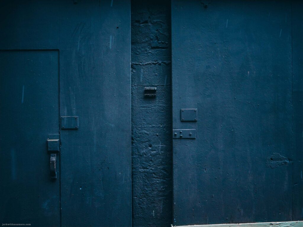 Dark blue painted wall with narrow metal door and textured surface