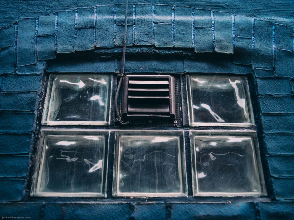 Close-up of a glass block window and vent set into a painted brick wall.